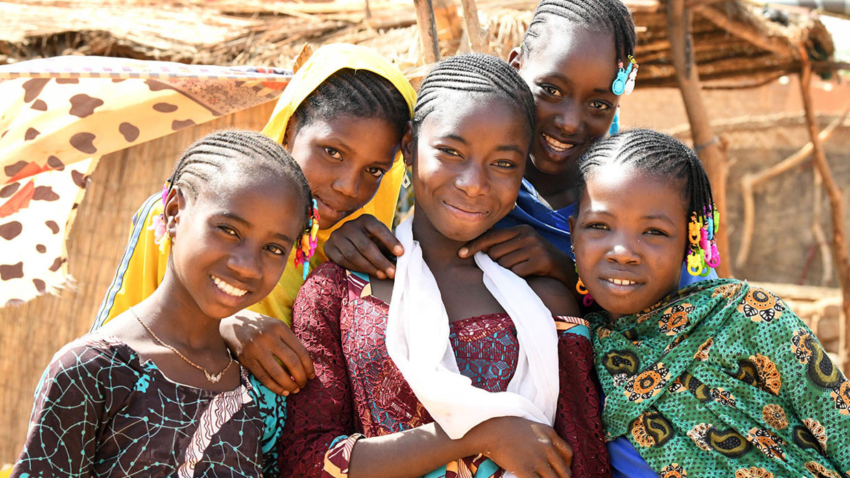 Photo of five girls in colorful clothing standing close together and smiling at the camera.