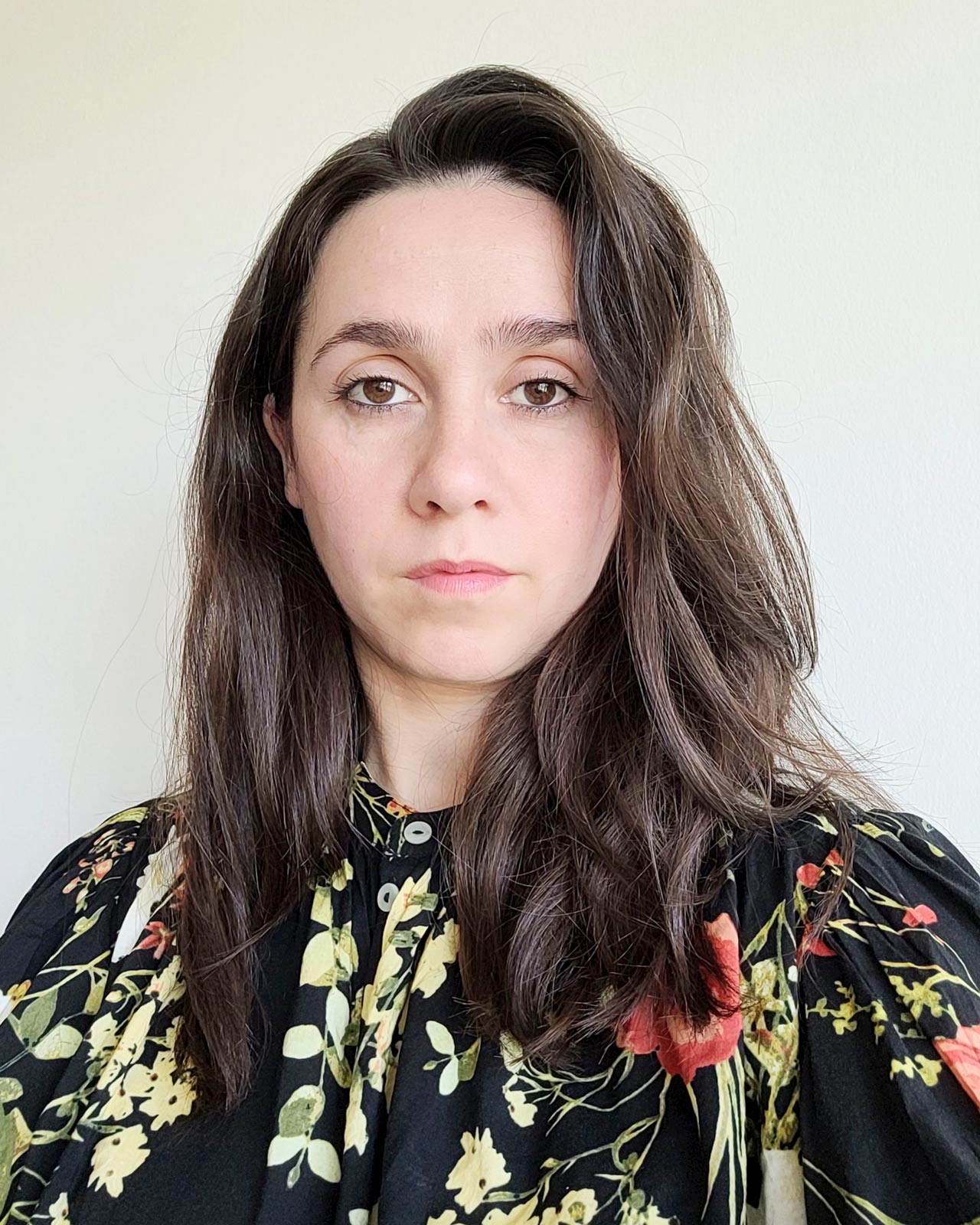 A headshot of artist Giselle Balosso-Bardin, collaborator on the 26SS limited collection. She has long brown hair and wears a floral blouse, looking forward with a gentle, focused gaze.