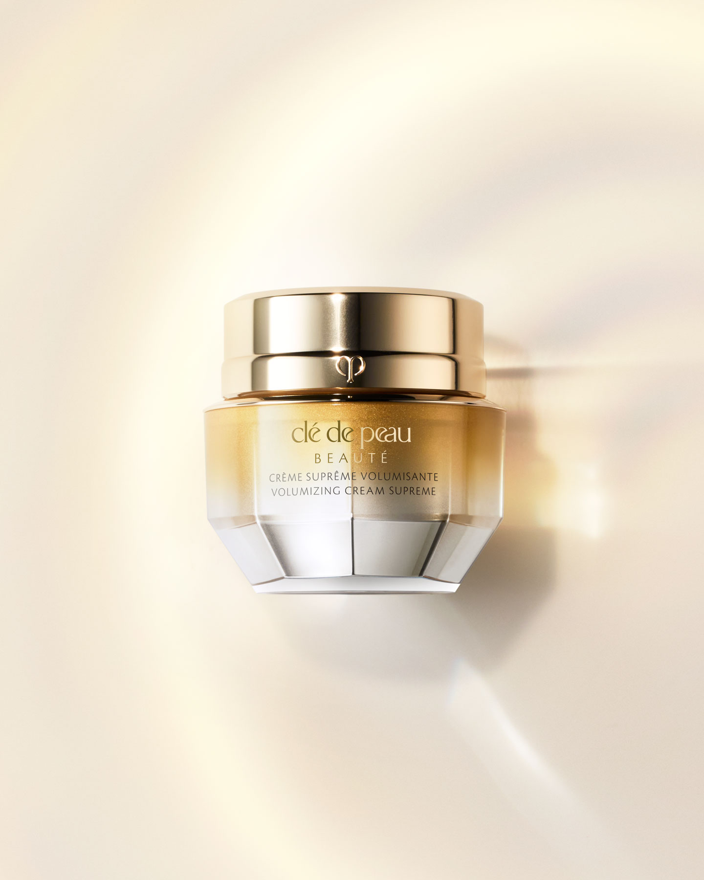 Photo of a VOLUMIZING CREAM SUPREME jar with a silver-to-gold gradient from top to bottom.