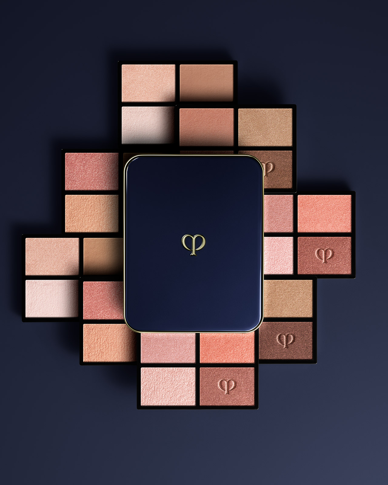 Photo of the EYE COLOR QUAD (REFILL) collection. A blue-black compact case is placed in the center, and refills in beige and brown tones are arranged in a radial pattern.