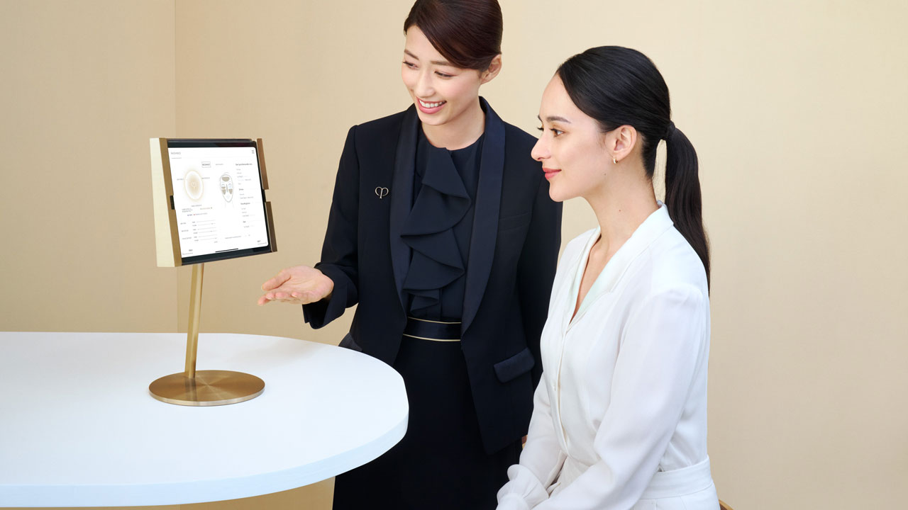Photo of a personal beauty specialist explaining skin analysis results to a woman while referring to a tablet on the table.