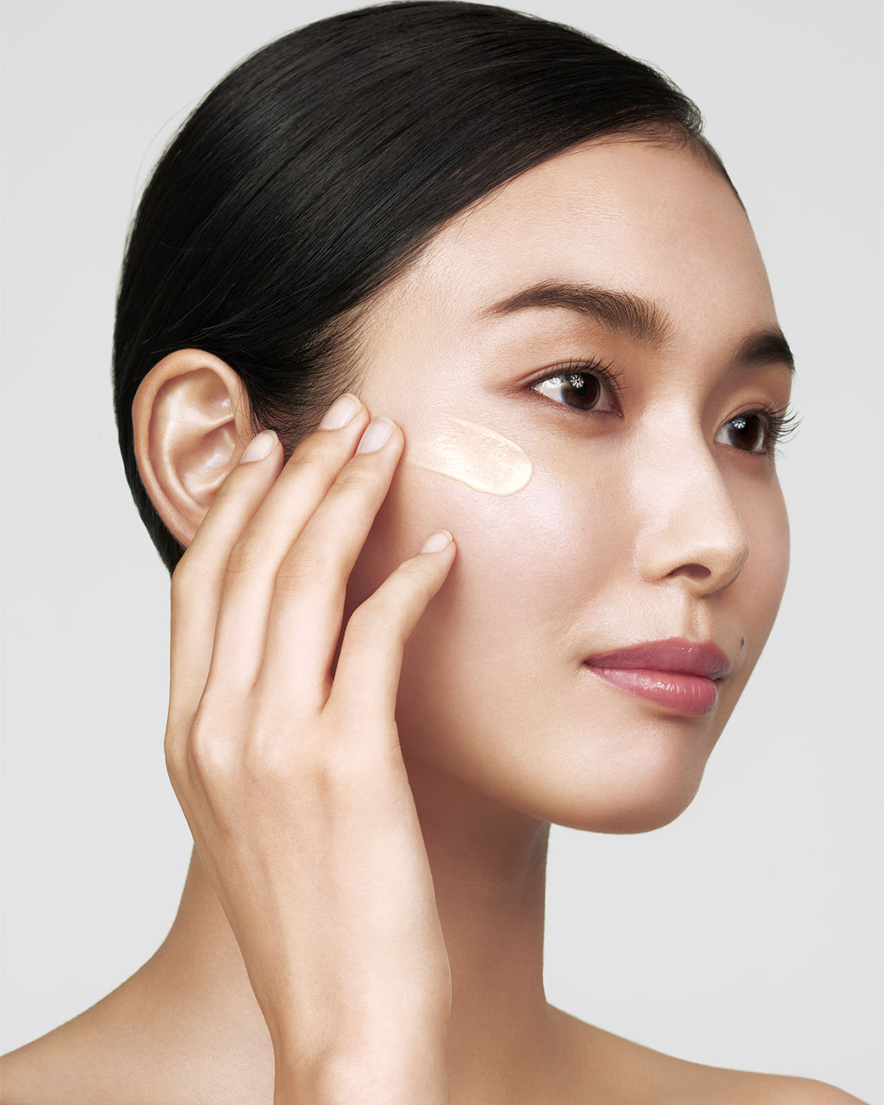 Photo of a medium skin tone model applying "WRINKLE SMOOTHING SERUM SUPREME" to the cheek.