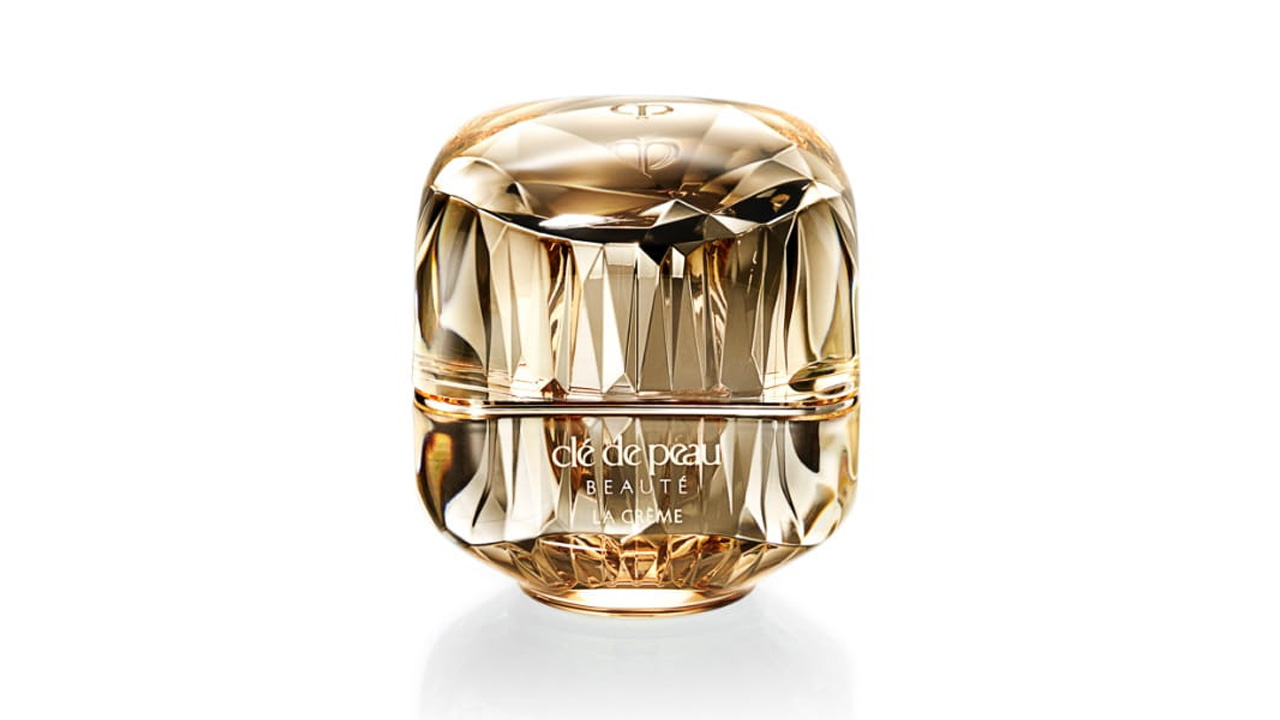 Photo of a jewel-cut, translucent gold container. The sparkling form reflects light, and the front features the brand logo and the text &ldquo;LA CR&Egrave;ME&rdquo; (current packaging).
