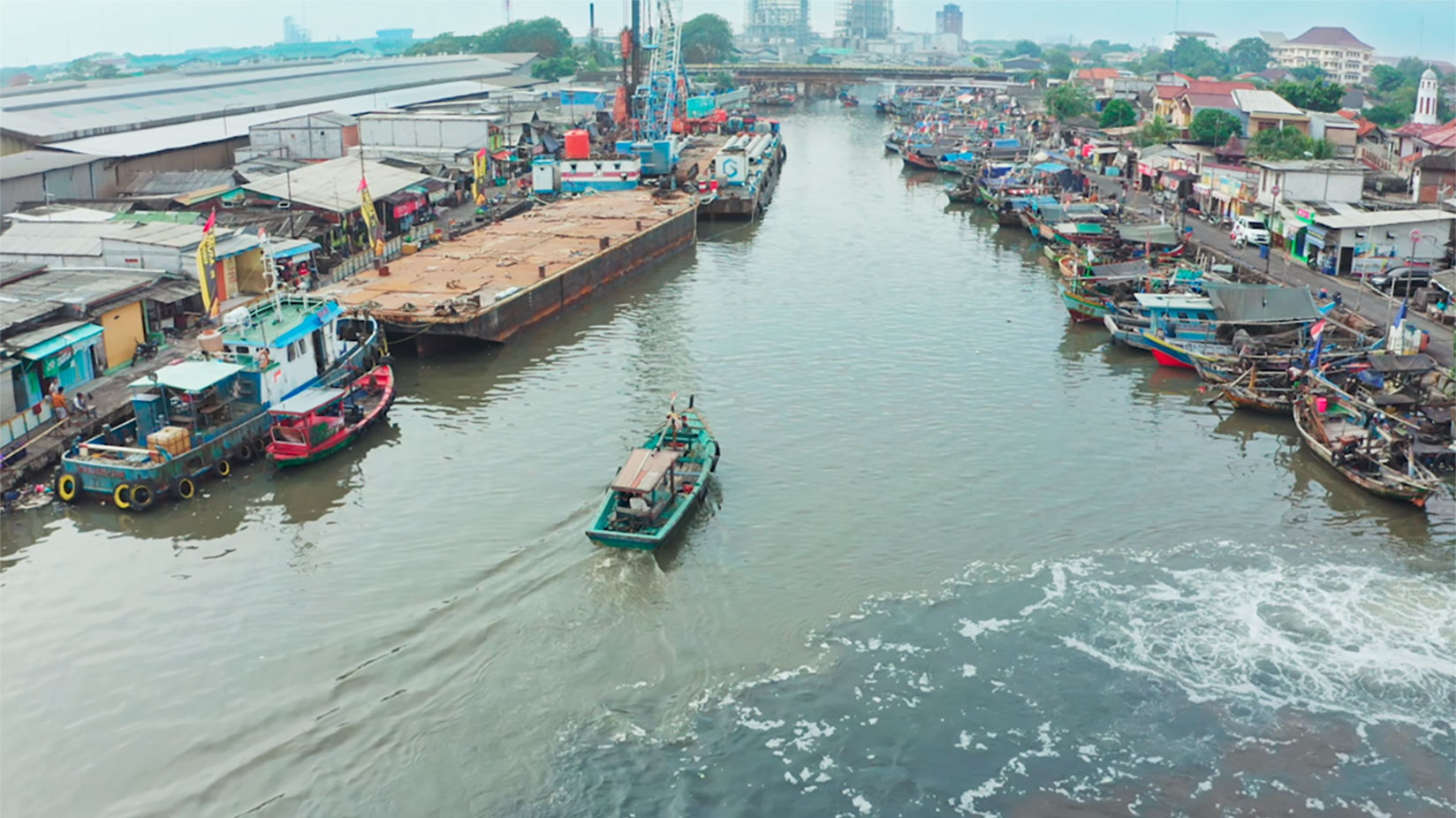 Photo of a fishing village in Cilincing, North Jakarta, showing boats and waterfront buildings along a river.