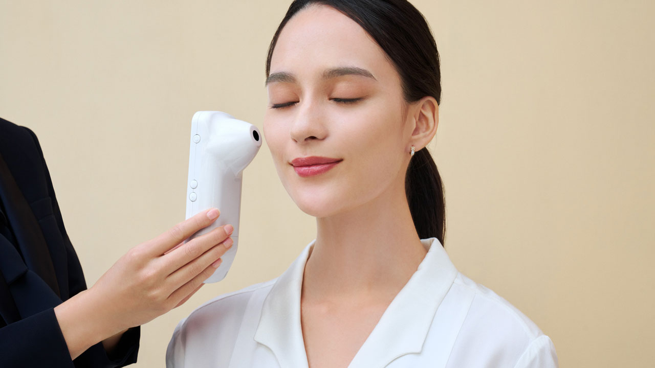 Photo of a Cl&eacute; de Peau Beaut&eacute; personal beauty specialist using a Handy Skin Sensor (HSS) to measure a customer&rsquo;s skin.