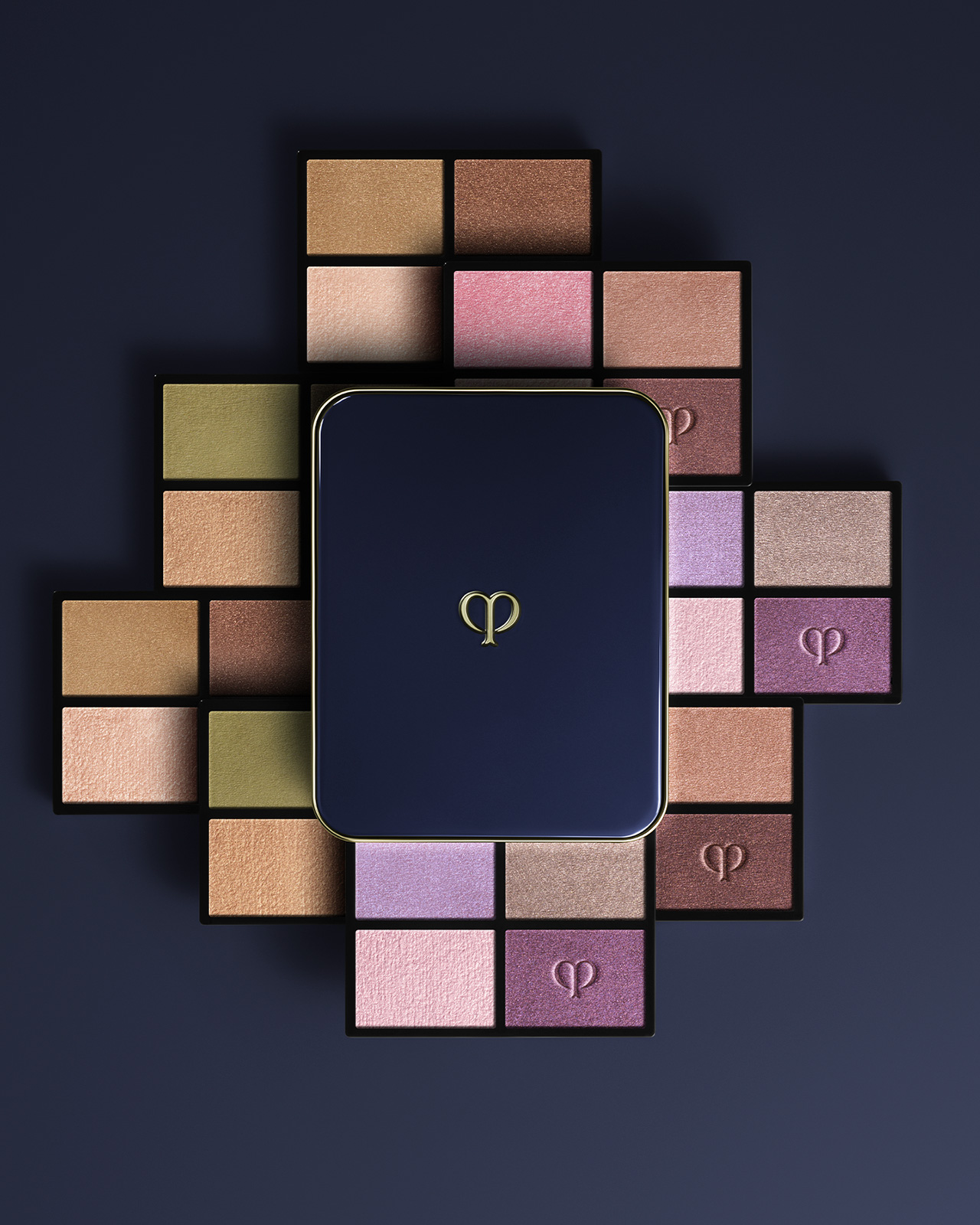 Photo of the EYE COLOR QUAD (REFILL) collection. A blue-black compact case is placed in the center, and refills in beige, purple, and brown tones are arranged in a radial pattern.