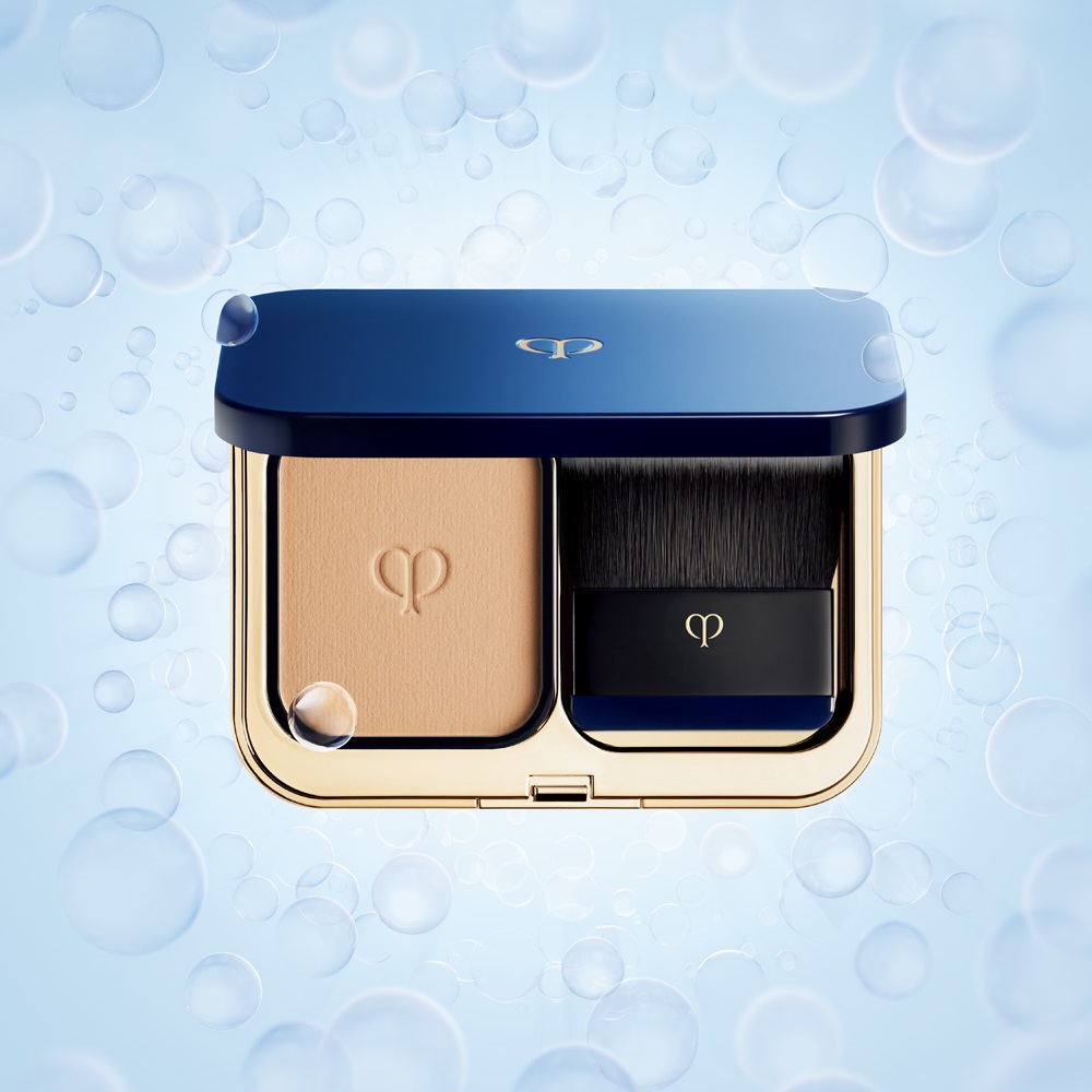 Photo of Cl&eacute; de Peau Beaut&eacute;&rsquo;s global brand ambassador, Nicole Kidman, wearing a black sleeveless dress and reclining gracefully on a sofa beside La Cr&egrave;me and The Foundation jars against a dark background.