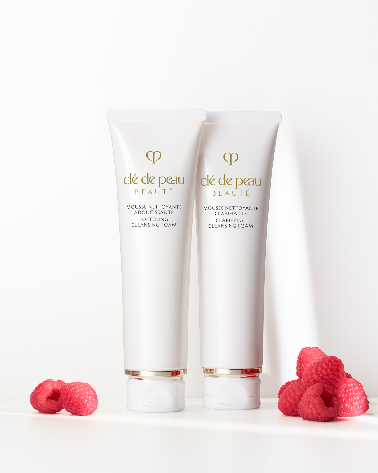 Photo of Cl&eacute; de Peau Beaut&eacute; SOFTENING CLEANSING FOAM and CLARIFYING CLEANSING FOAM tubes displayed with fresh raspberries, representing the raspberry extract used in both products.