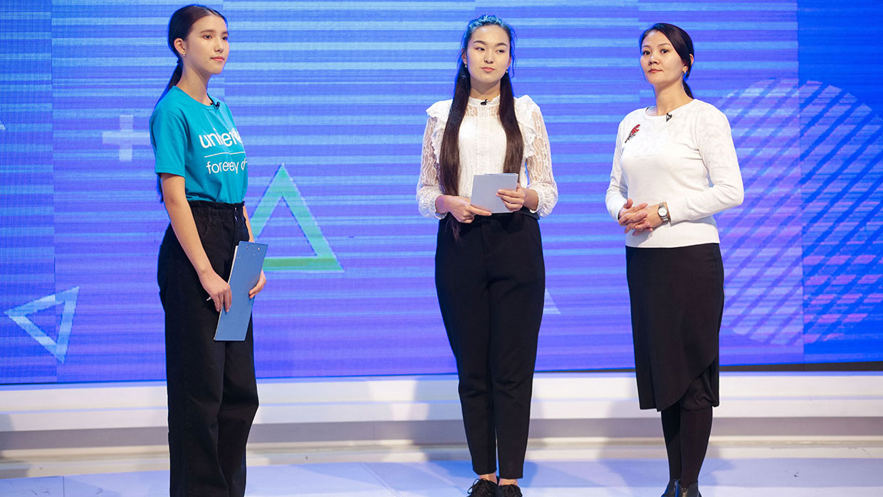 Photo of three women standing on a stage during a presentation or event.