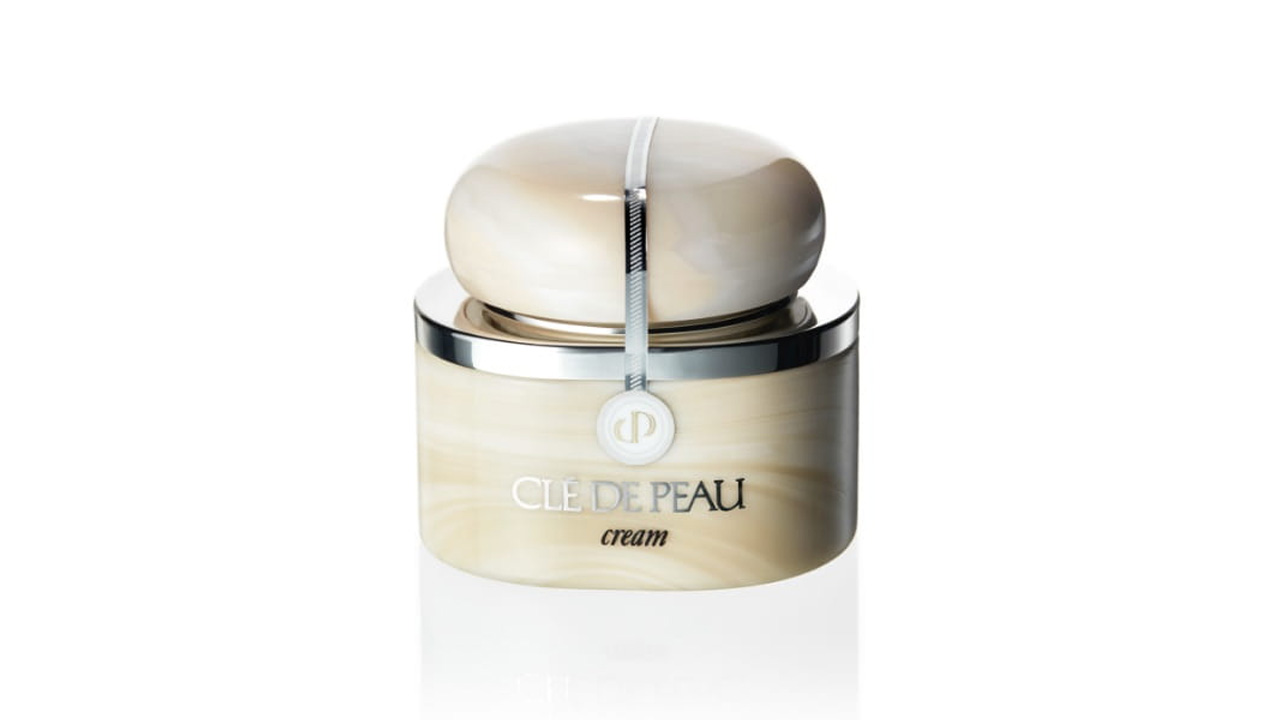 Photo of a beige container with a marble-like texture, featuring a rounded cap accented by a silver line. The front displays the brand logo and the product name &ldquo;cream&rdquo; (former packaging).