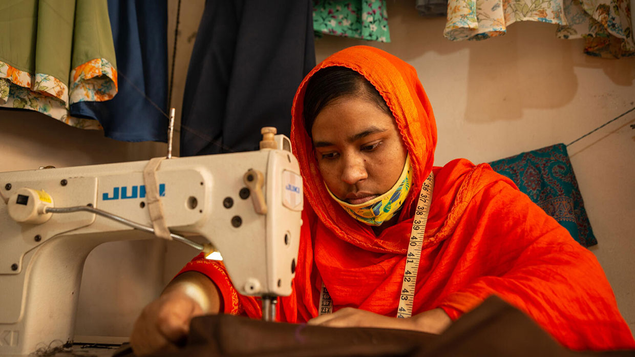 Photo of a woman wearing an orange headscarf, focused on sewing with a machine.