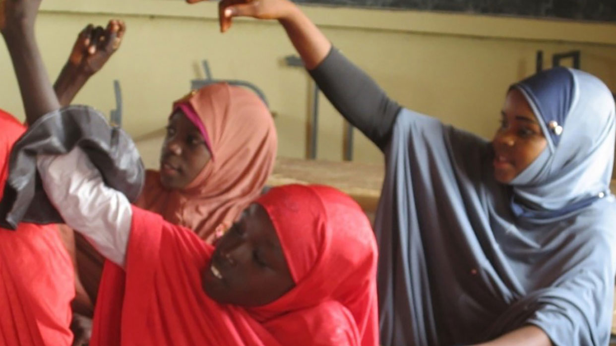 Photo of girls in headscarves raising their hands in a classroom setting.