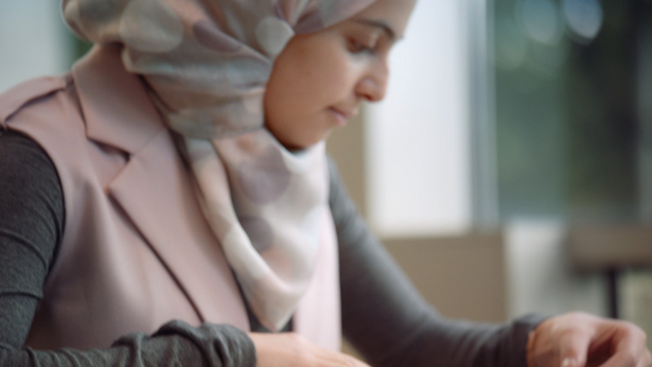 Photo of Muzoon Almellehan wearing a light-colored hijab, looking down as she reads or writes during a quiet moment.