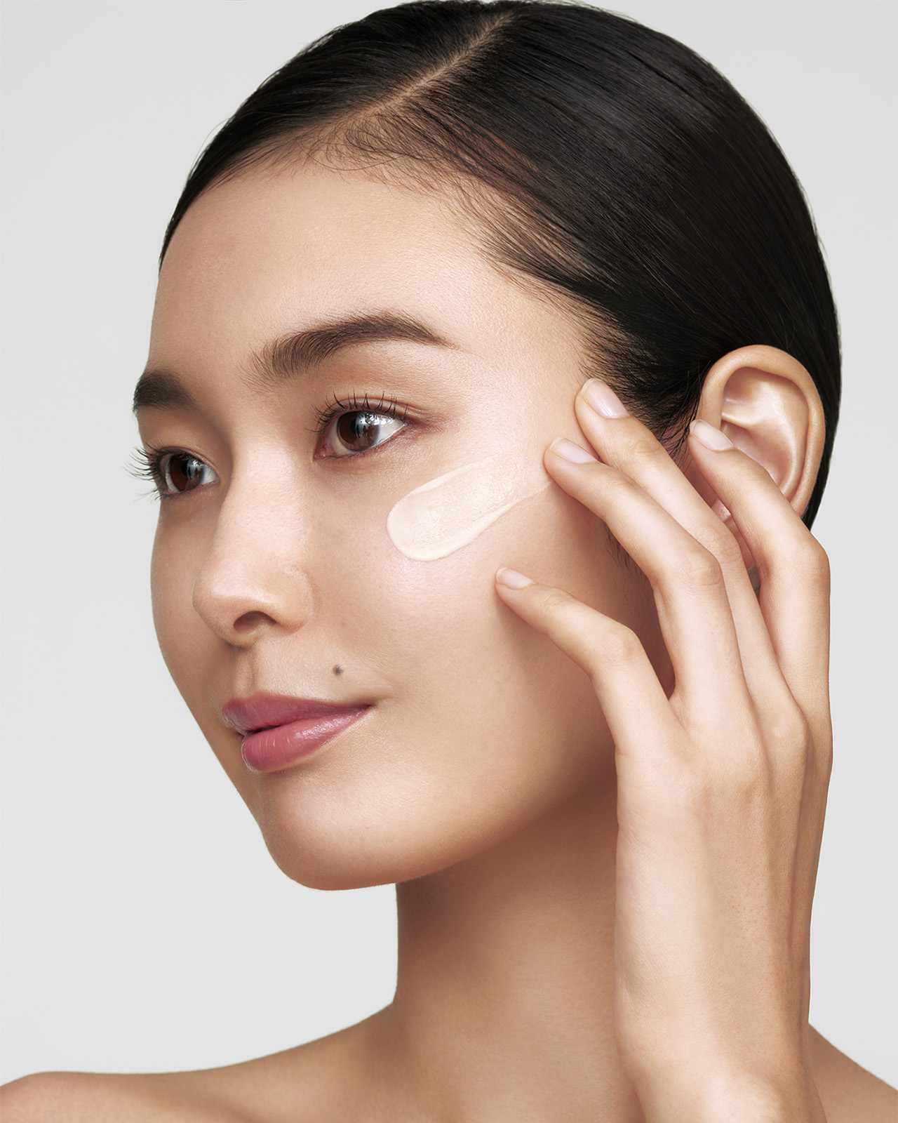 Photo of a medium skin tone model applying "FIRMING SERUM SUPREME" to the cheek.