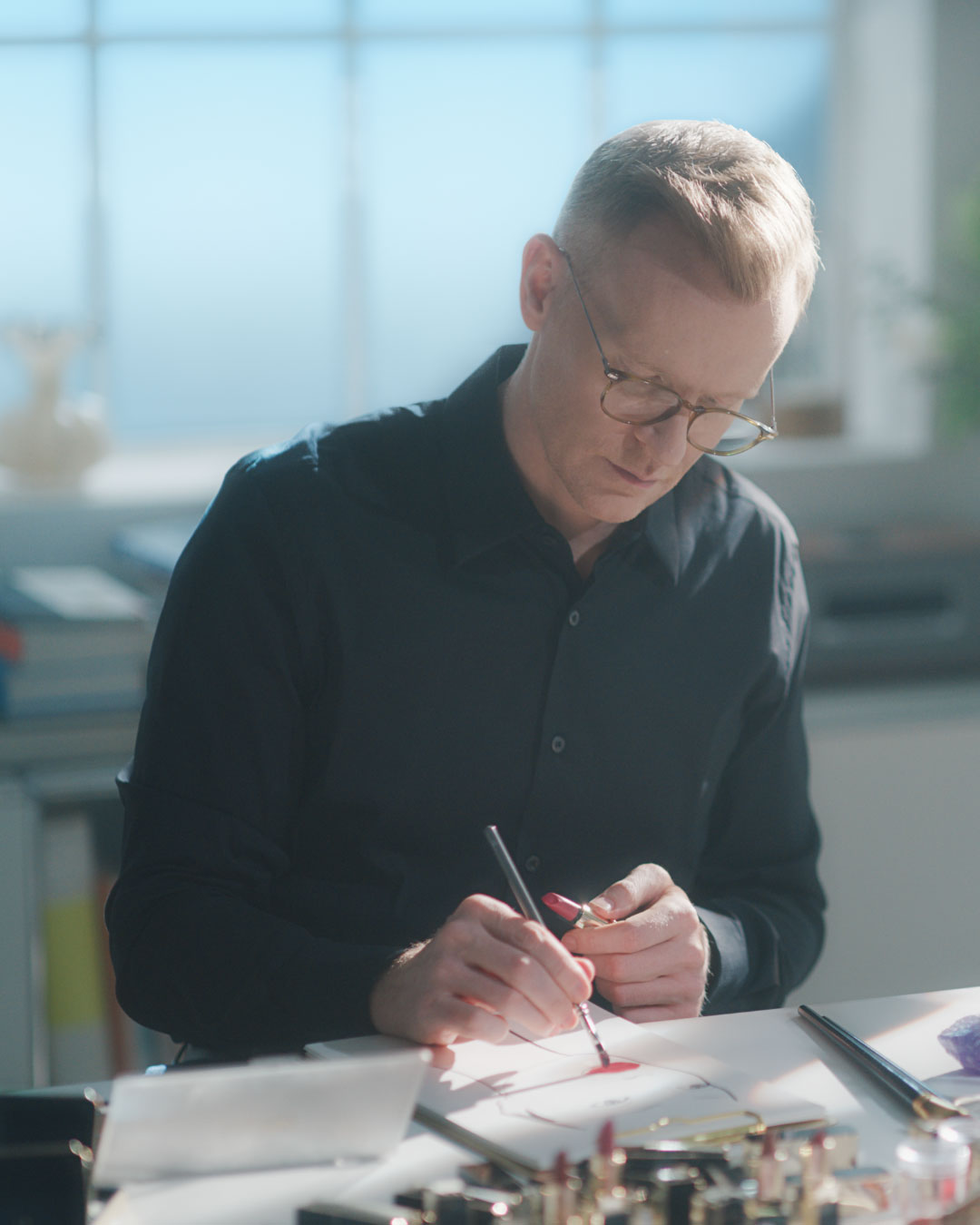 PPhoto of Benjamin Puckey, wearing glasses and a dark shirt, concentrating on a drawing with a brush pen at a desk.