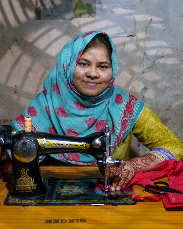 Photo of a woman wearing a scarf, sewing red fabric on a sewing machine.