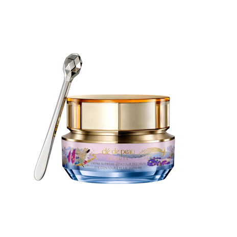 Photo of the 26 AW Holiday Collection limited-edition EYE CONTOUR CREAM SUPREME. The gold-trimmed jar features a blue and pink pastel illustration with a gold shooting star, shown beside a faceted silver spatula.