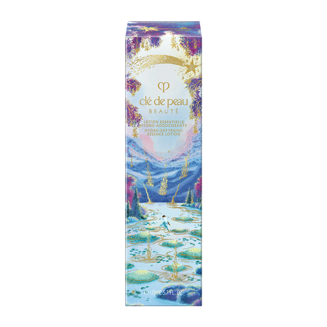 Photo of the 26 AW Holiday Collection limited-edition HYDRO-SOFTENING ESSENCE LOTION outer box. The package shows a person stepping on stones across a blue lake with gold ripples, decorated with a gold shooting star and purple trees at the top.