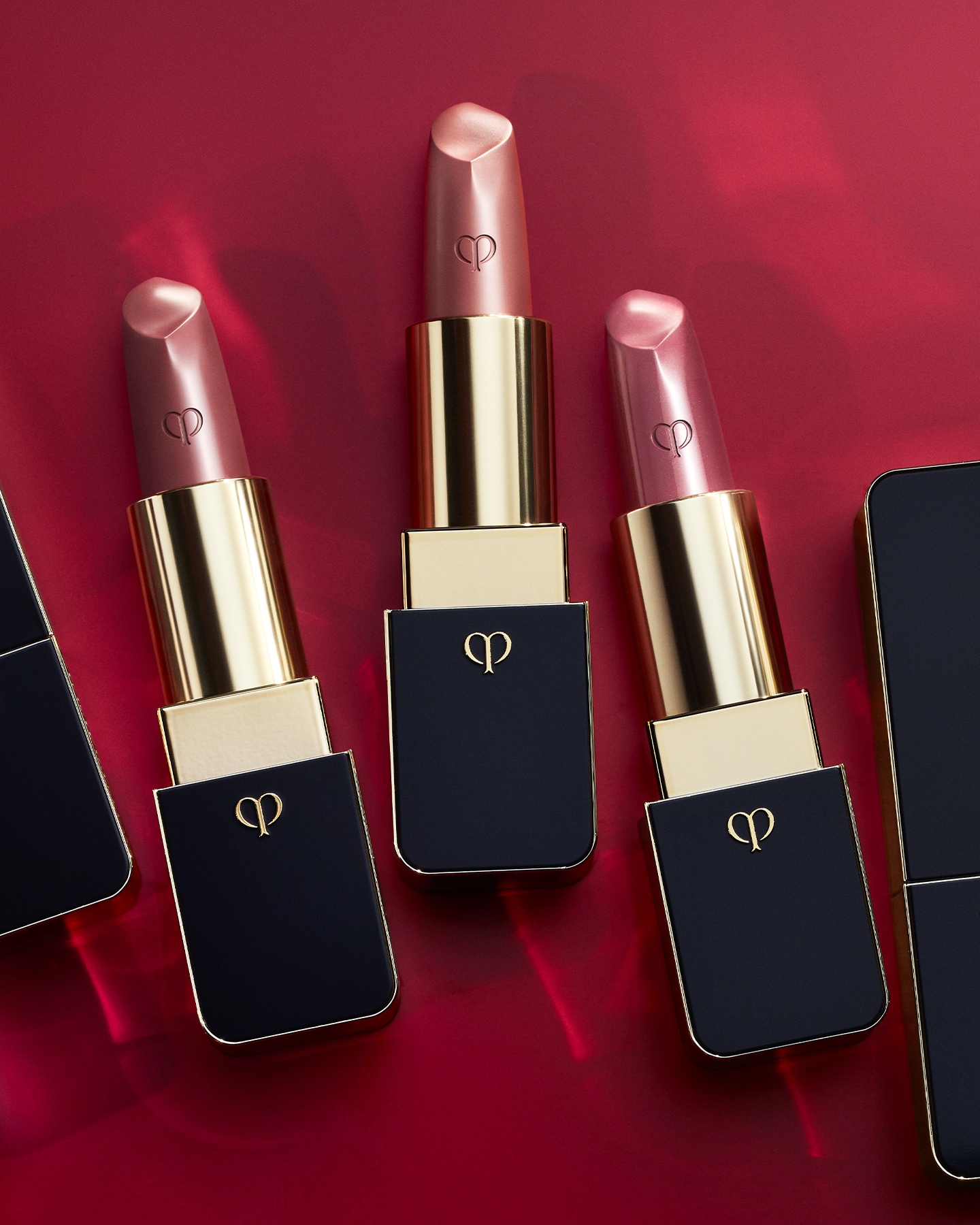 Photo of three "LIPSTICK" products arranged side by side on a red background. The caps are removed to clearly display each shade.